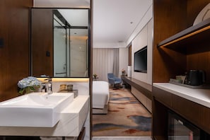 A modern hotel room with a large white sink, a bed with a white headboard, a TV mounted on the wall, and a small table with a vase of flowers. - Madison Hotel Hefei 2nd Affiliated Hospital (Hefei)