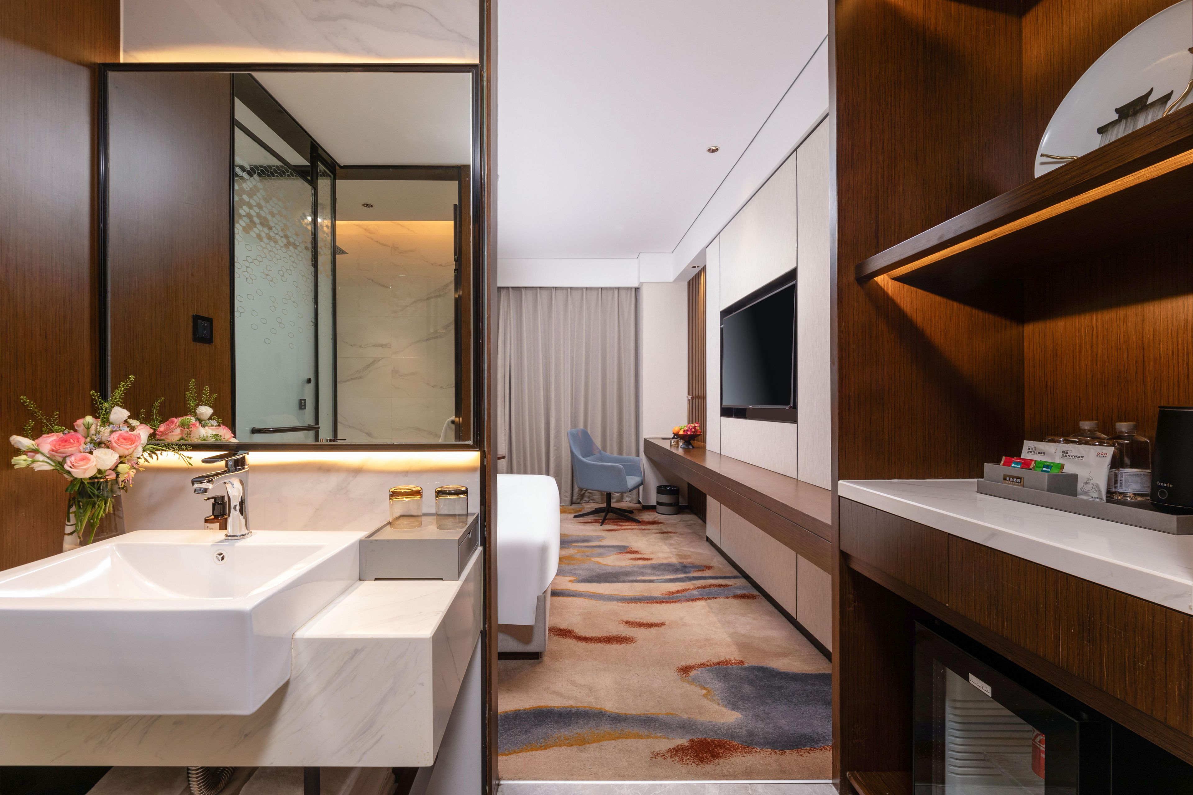 Un bany d'hotel modern amb un mirall gran, un lavabo blanc i una zona de dutxa.