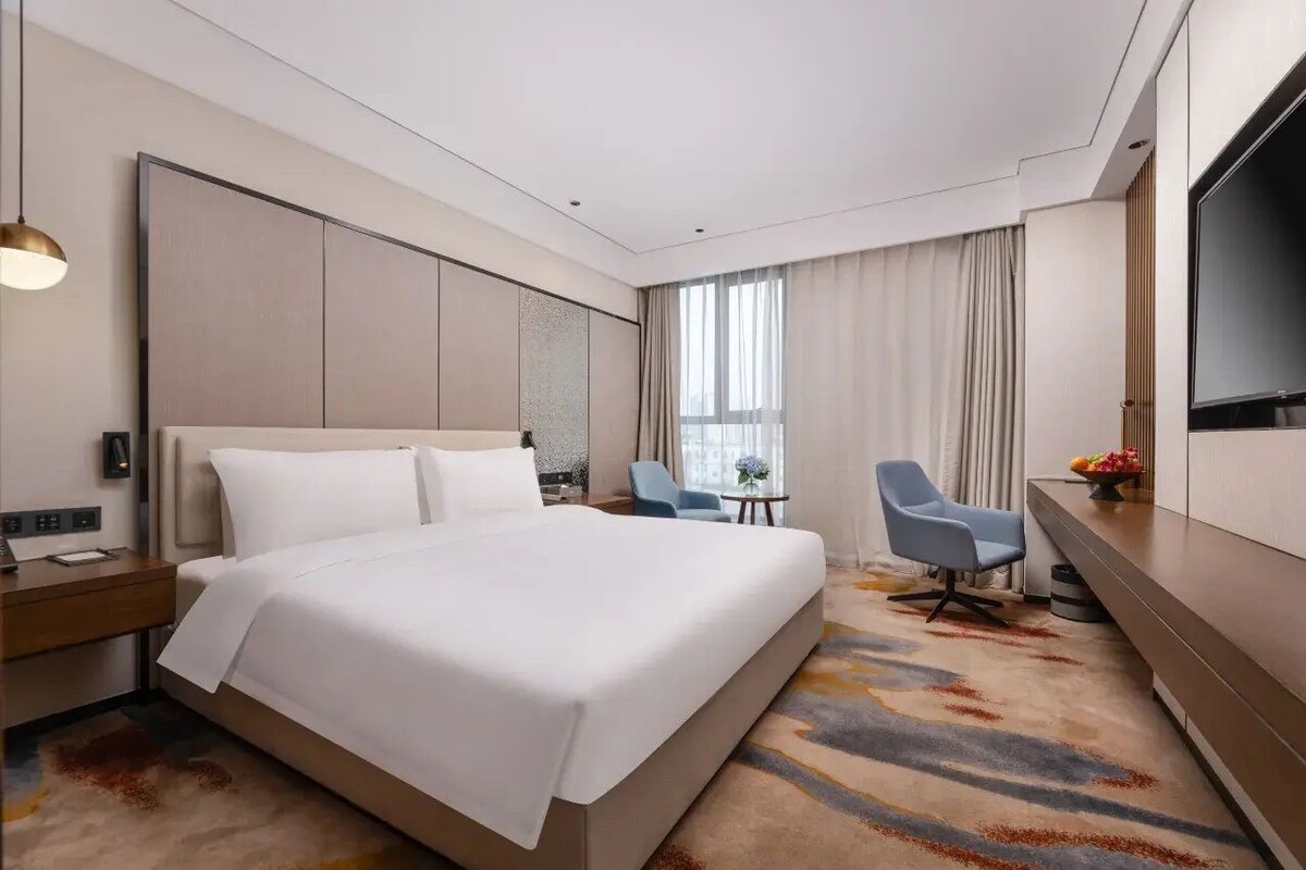 A modern hotel room with a large bed, a desk, a chair, and a TV.
