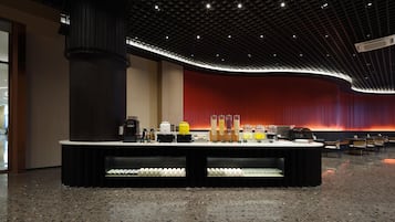 Un lobby moderno con una pared curva roja, una columna negra central y una zona de bar con diversos elementos.