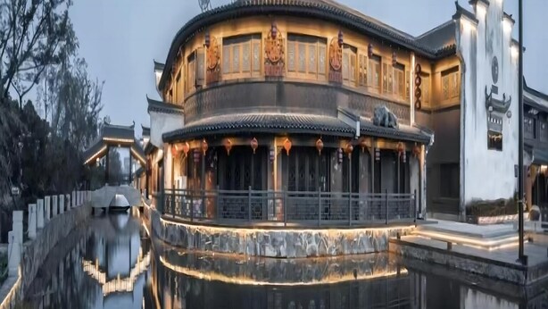 Un edificio tradicional con fachada curva y su reflejo en el agua, además de un asta de banderas.