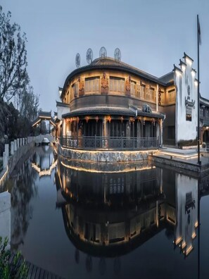 Un bâtiment traditionnel à la façade incurvée, qui se reflète dans l’eau, et sur lequel flotte un drapeau.