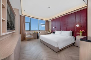 Una habitación de hotel moderna con una cama grande, un escritorio y una silla. Se ve una ventana con vista al cielo.