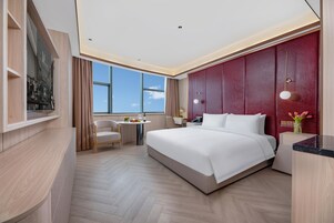 Una habitación de hotel moderna con una cama grande, un escritorio y una silla. Se ve una ventana con vista al cielo.