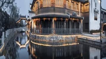 Un edificio tradicional con fachada curva y su reflejo en el agua, además de un asta de banderas.