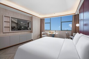 Habitación de hotel moderna con una cama grande, una mesa redonda de comedor, una zona de estar y un ventanal con vistas.