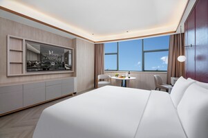Habitación de hotel moderna con una cama grande, una mesa redonda de comedor, una zona de estar y un ventanal con vistas.