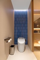 Un baño moderno con inodoro, un cesto de basura y una repisa con un rollo de papel higiénico.