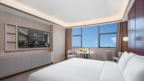 Una habitación de hotel moderna con una cama grande, una mesa de comedor, una silla y un televisor instalado en la pared.