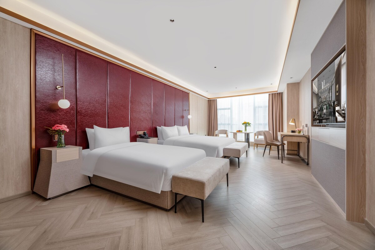 Ein modernes Hotelzimmer mit zwei Betten, einem Schreibtisch und Blick auf die Stadt.