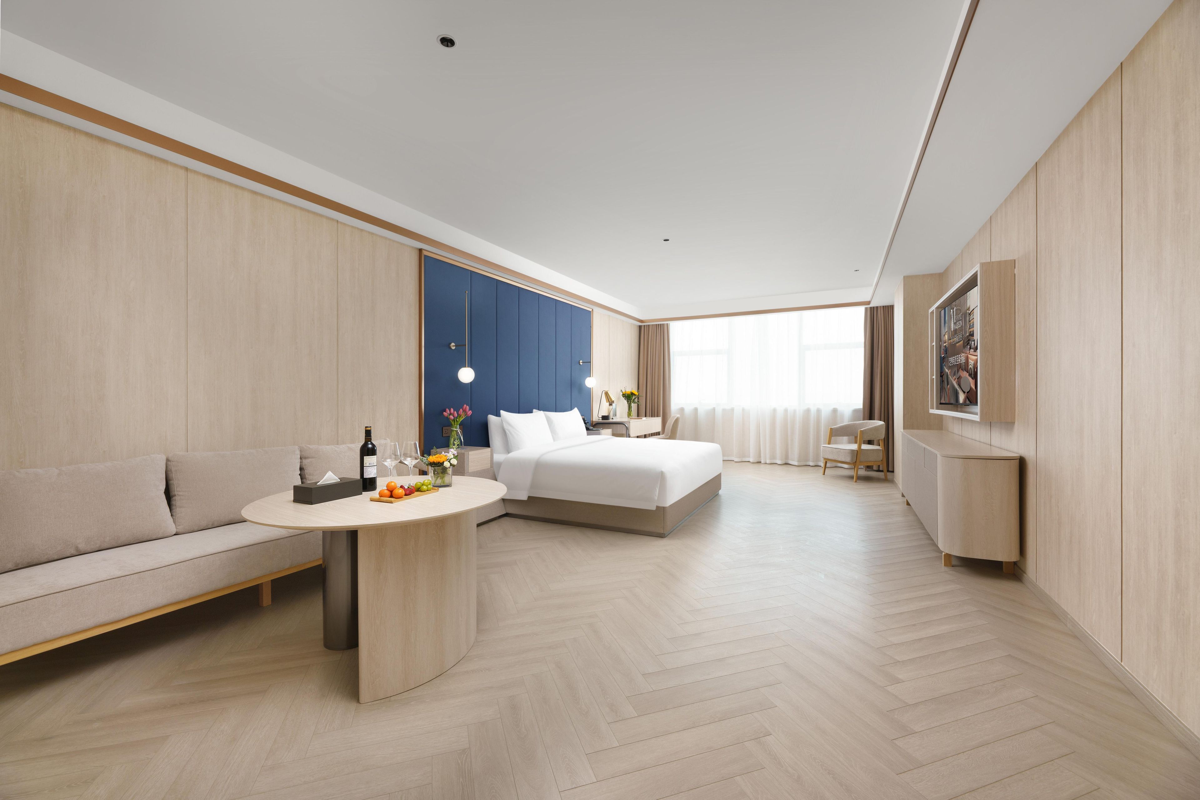 Ein modernes Hotelzimmer mit einer Couch, einem Bett, einem Esstisch und einem Einbauschrank.