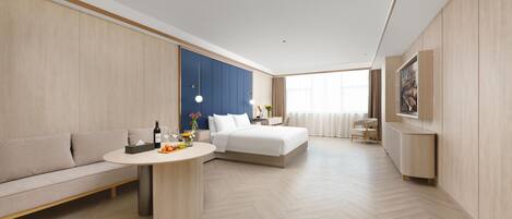 A modern hotel room with a sofa, a bed, a dining table, and a built-in wardrobe.