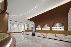 Un moderno vestíbulo de hotel con un mostrador de recepción de mármol, una zona de estar y una gran pared curva con pantalla digital.