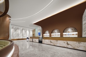 Un moderno vestíbulo de hotel con un mostrador de recepción de mármol, una zona de estar y una gran pared curva con pantalla digital.