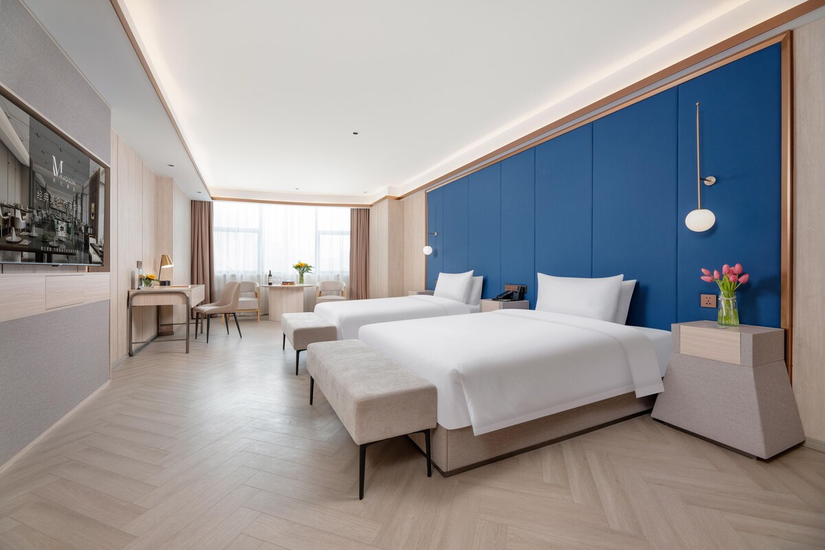 Una habitación de hotel moderna con dos camas, un escritorio y un ventanal grande.