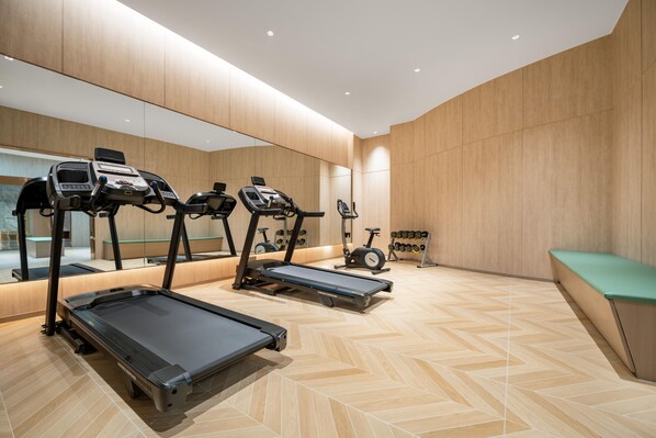 Une salle de sport moderne équipée de tapis de course, de vélos d’appartement et d’un mur recouvert de miroirs.
