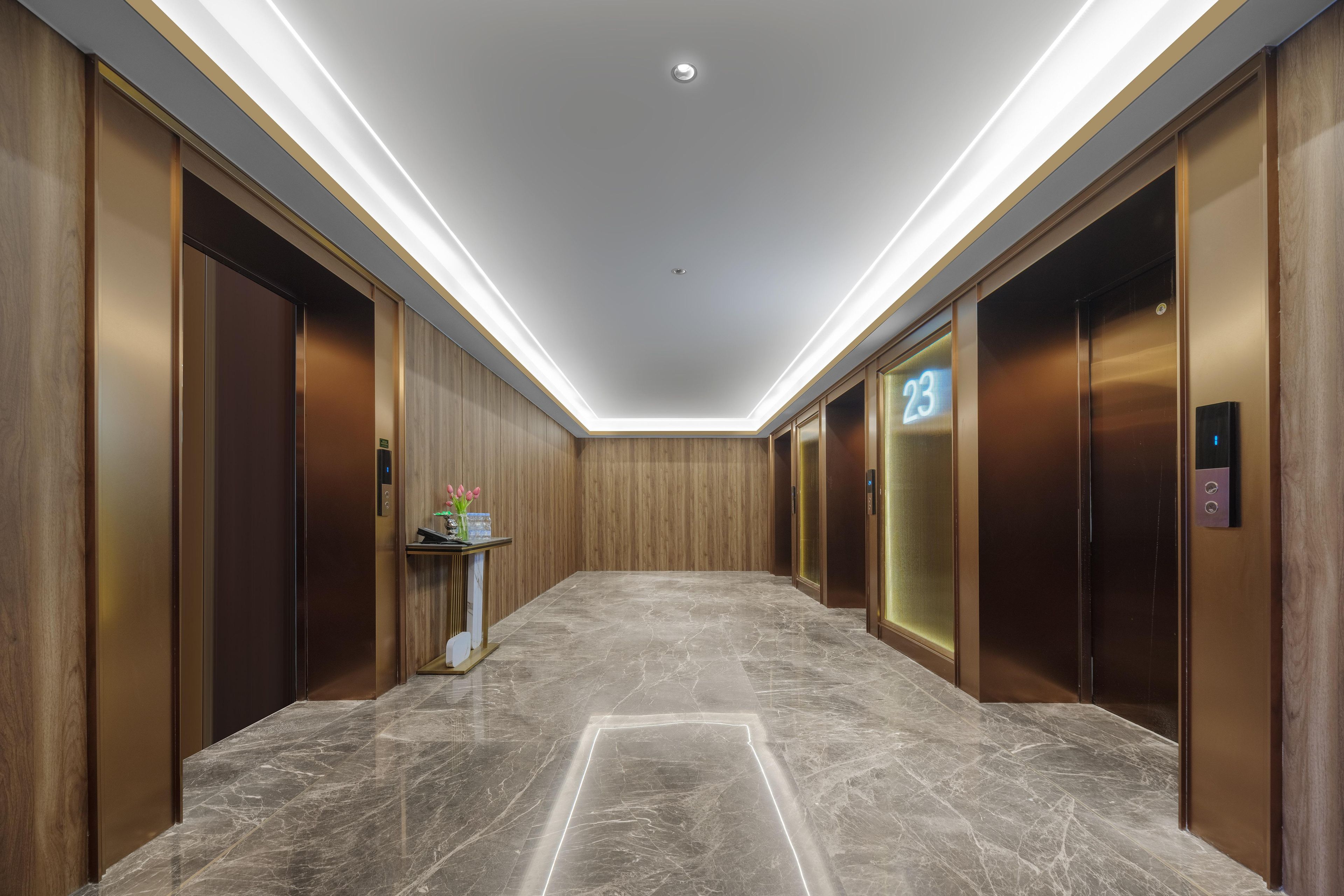 A modern hallway with marble flooring, wooden paneling, and two elevators, one marked with the number 23.