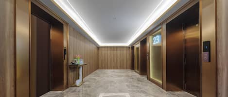 Un pasillo moderno con suelo de mármol, paneles de madera y dos ascensores, uno de ellos con el número 23.