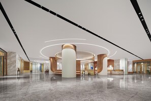 Un lobby amplio con una zona de estar circular central, mostrador de recepción y un diseño moderno con pisos de mármol y detalles de madera.