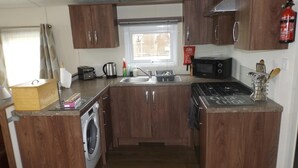 Una cocina compacta con armarios de madera, un lavamanos de acero inoxidable, microondas, tostadora y estufa a gas.