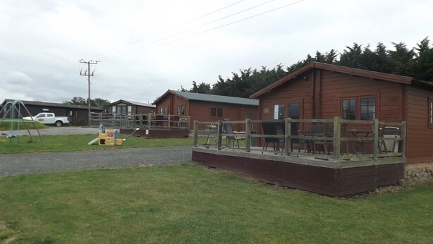 A wooden cabin with a deck, a swing set, and a picnic table. - Spacious 3 bedroom cabin at Avonvale Holiday Lodge (Evesham)