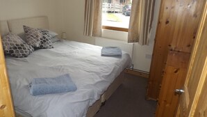 Une chambre à coucher avec un lit, des oreillers, une fenêtre avec des rideaux, un radiateur et une porte en bois.