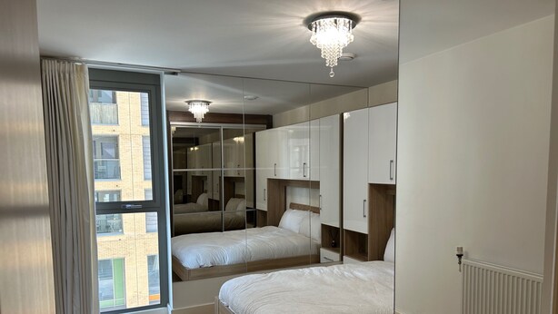 A modern bedroom with two beds, a large wardrobe, and a view through a sliding door. - 1-Bed Apt, Sleeps 4, Central To Shops & Transport (London)