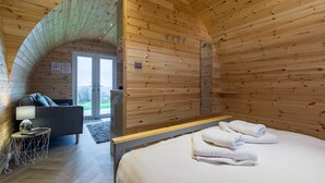 A wooden cabin room with a bed, a sofa, a small table, and a shower area. - The Lodge at Brambles Farm - Sleeps 4, Hot Tub (Leek)
