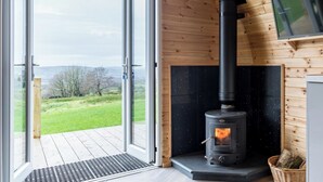 A modern log cabin with a glass door leading to a deck, a black wood-burning stove, and a television mounted on the wall. - The Lodge at Brambles Farm - Sleeps 4, Hot Tub (Leek)