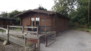 A wooden cabin with a covered deck and a gravel driveway.