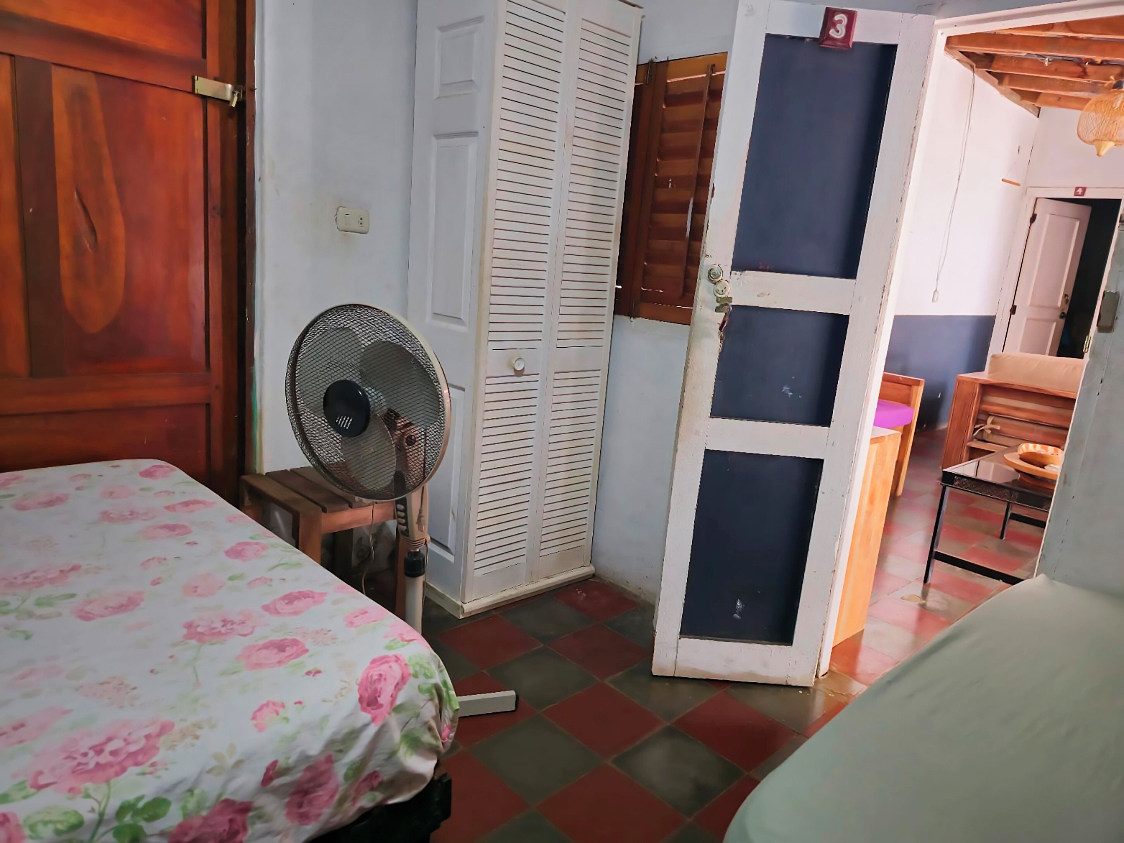 Una habitación con una cama, un ventilador, un armario y una puerta que da a otra habitación.