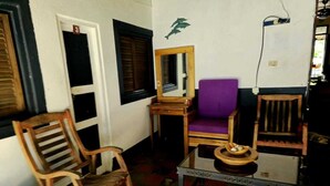 Une pièce comprenant une chaise en bois, un fauteuil violet rembourré, une petite table avec un bol, un miroir et une prise électrique fixée au mur.