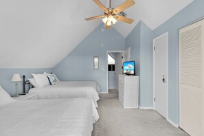 Two single beds with white bedding and decorative pillows are featured in this cozy room, complete with a ceiling fan and mounted television.