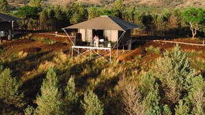 Alojamiento al aire libre apartado con un espacio de estar cubierto, rodeado de paisaje natural y colinas lejanas.