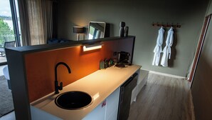 Cocina moderna con un lavabo, una cafetera y un espejo. Hay toallas colgadas en un perchero y vistas al exterior a través de amplias ventanas.