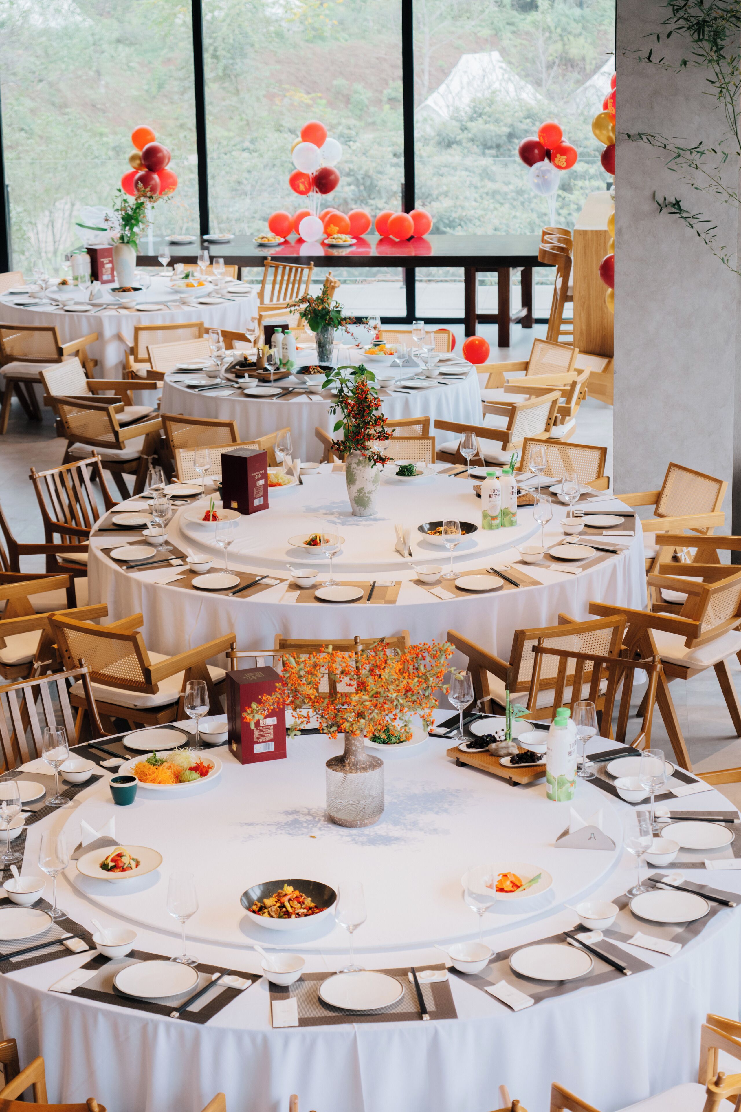 Un espace de restauration à plusieurs niveaux, avec des tables rondes, des chaises en bois et une vue sur la verdure environnante.
