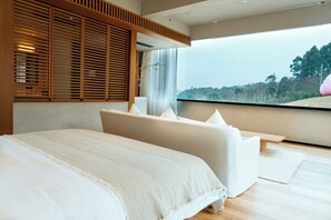 Une chambre à coucher moderne, dotée d’un grand lit, d’un canapé et offrant une vue sur une forêt grâce à une grande fenêtre.