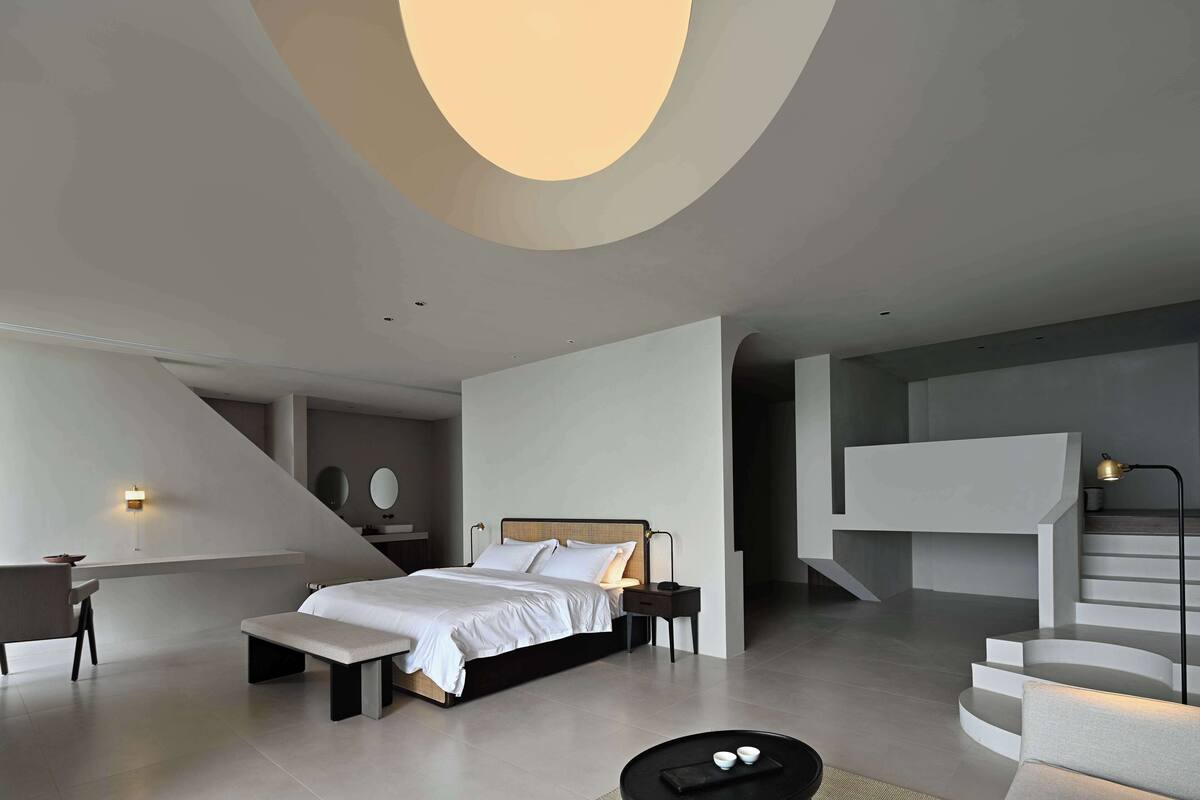 A modern bedroom with a bed, bedside tables, a desk, and a staircase.