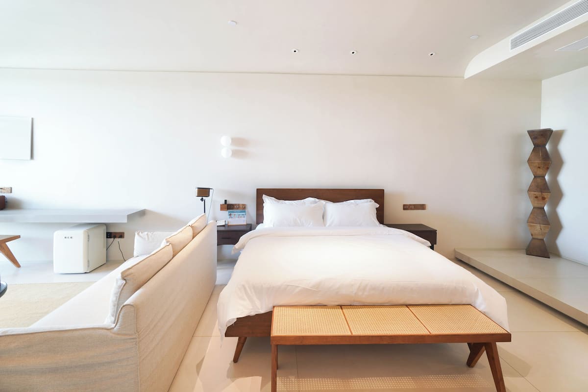 A modern bedroom with a large bed, bedside tables, a bedside lamp, a wall-mounted shelf, and a standing lamp.