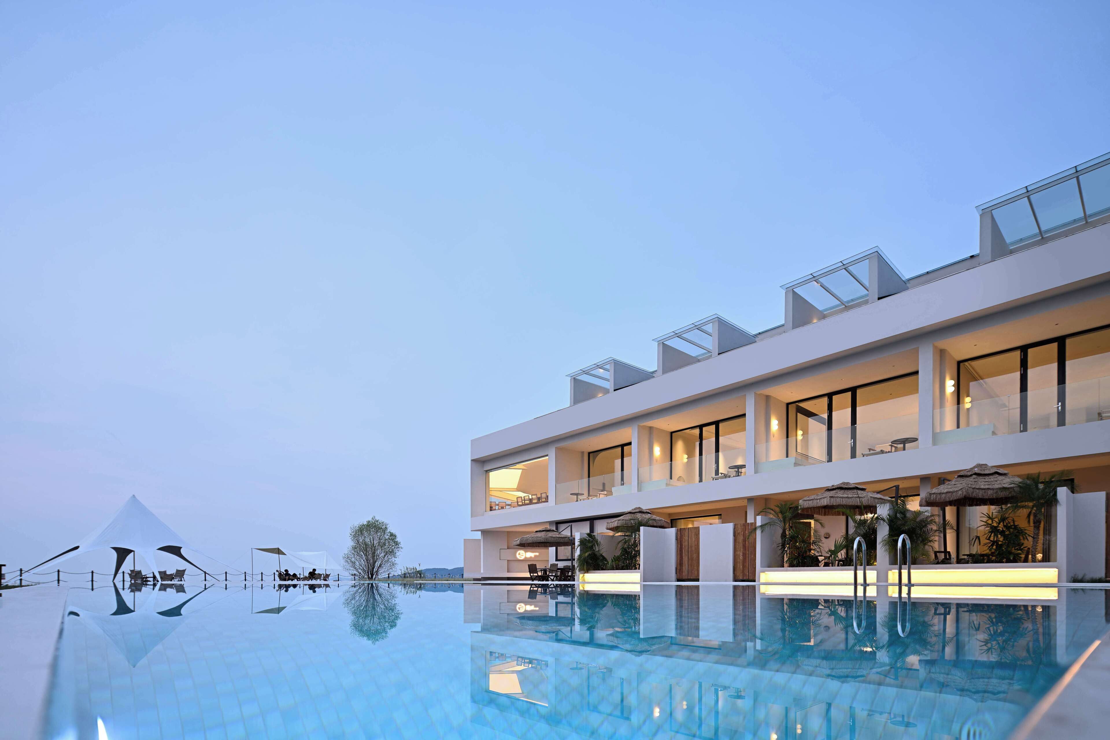 Un hotel moderno con piscina en la azotea, mobiliario exterior y una vista despejada del cielo.