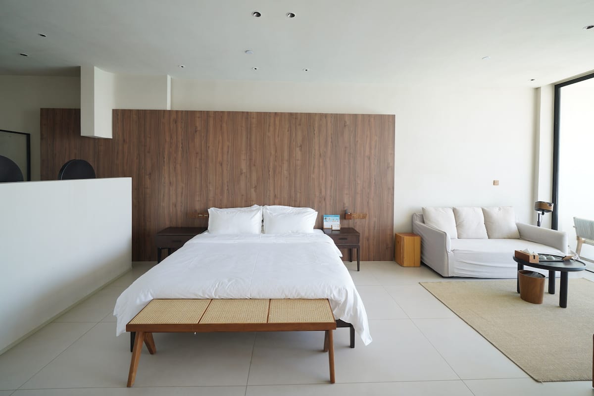 A modern bedroom with a large bed, a sofa, a small table, and a view of the outdoors.