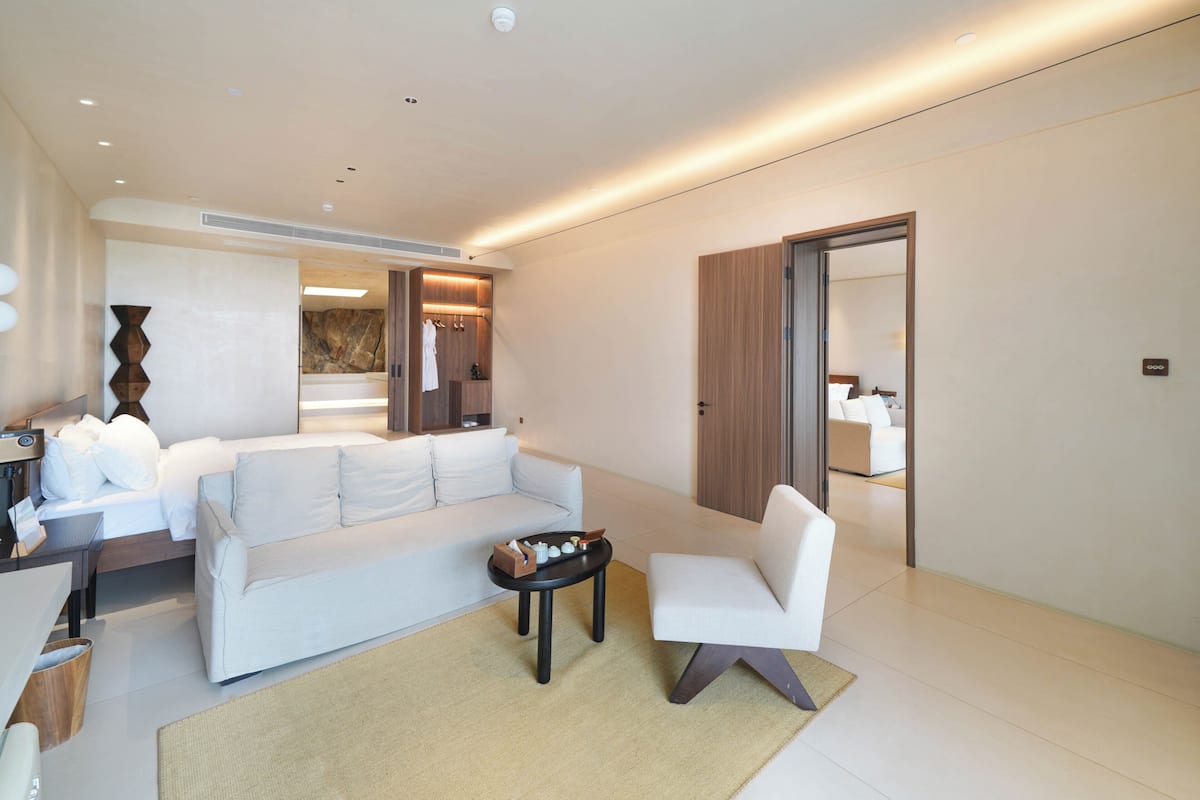 A modern hotel room with a large white sofa, a small round table, and a separate armchair.
