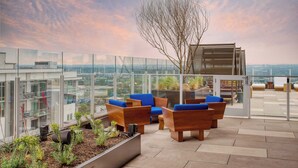 A rooftop terrace with wooden furniture, glass railings, and a view of the cityscape. - New Austin High Rise Near DT Luxe Amenities, Rooftop Pool, Gym+yoga Studio (Austin)