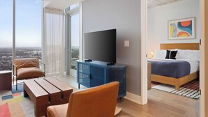 A modern hotel room with a large window, a flat-screen TV, a bed, and a seating area with a colorful rug. - New Austin High Rise Near DT Luxe Amenities, Rooftop Pool, Gym+yoga Studio (Austin)