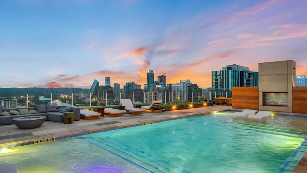 A rooftop pool with lounge chairs and a city skyline view at dusk. - New Austin High Rise Near DT Luxe Amenities, Rooftop Pool, Gym+yoga Studio (Austin)