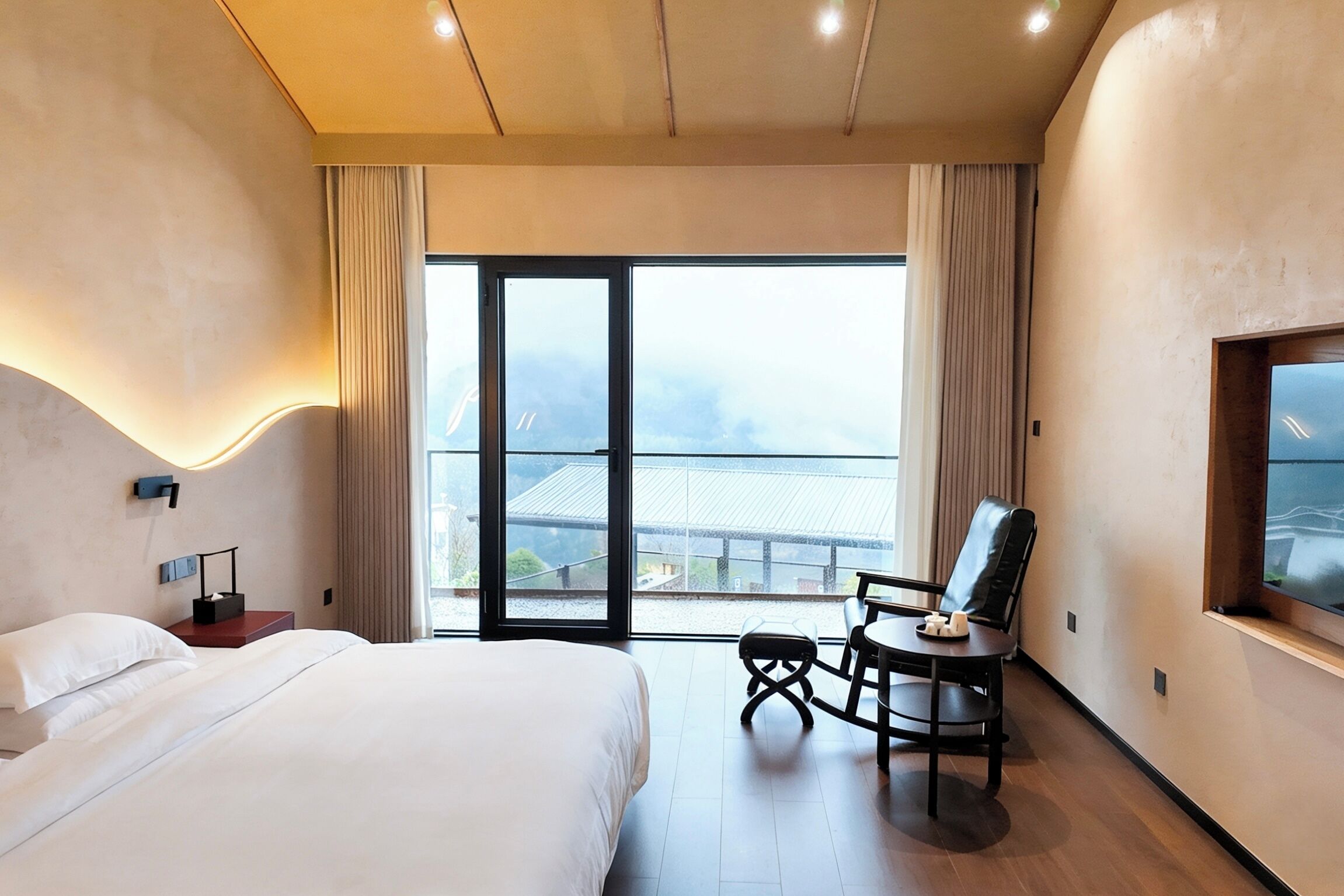 Una habitación de hotel con cama, escritorio con silla, ventana con cortinas y vista a un edificio.
