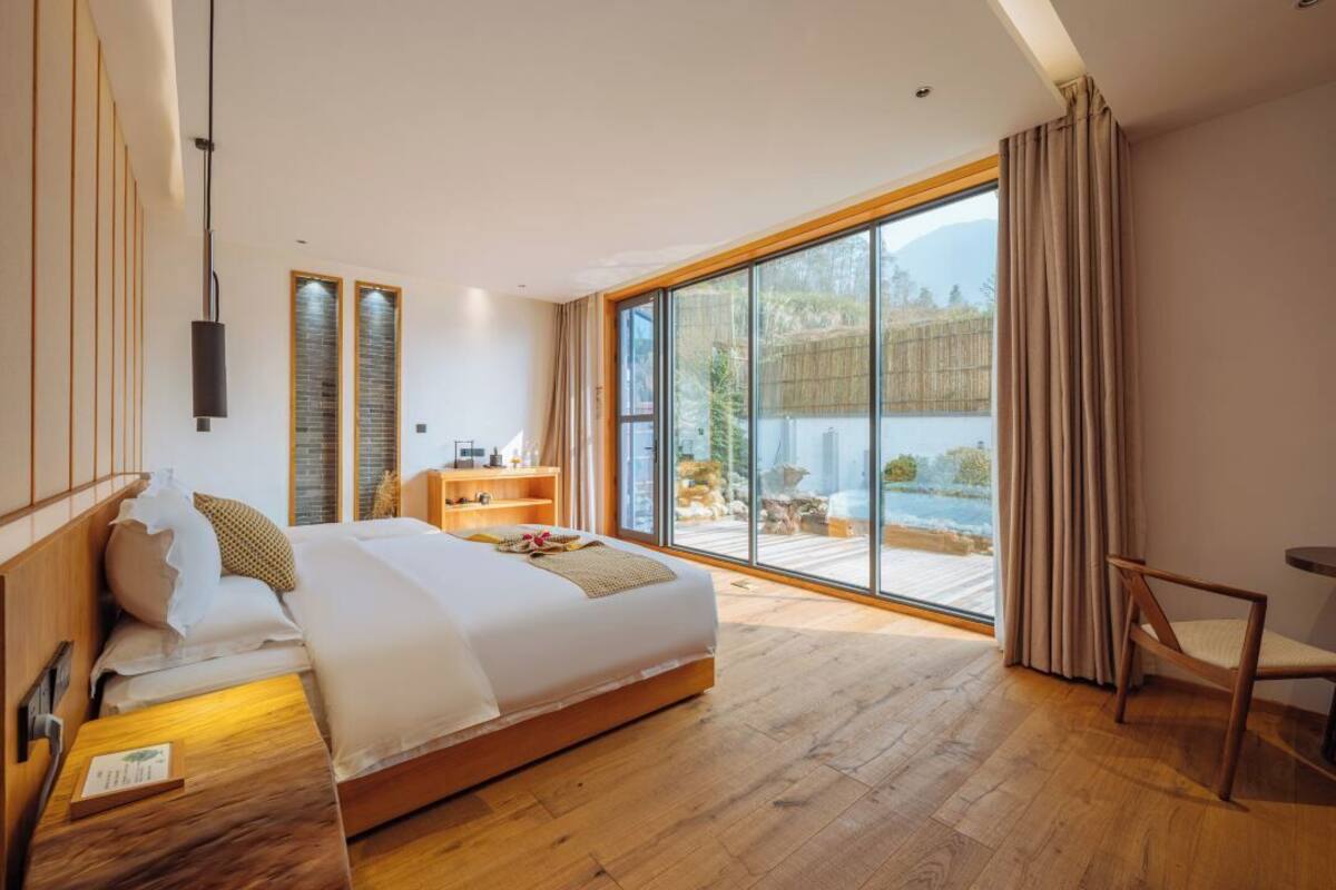 A modern bedroom with a large bed, wooden headboard, and a view of a mountain landscape through floor-to-ceiling windows.