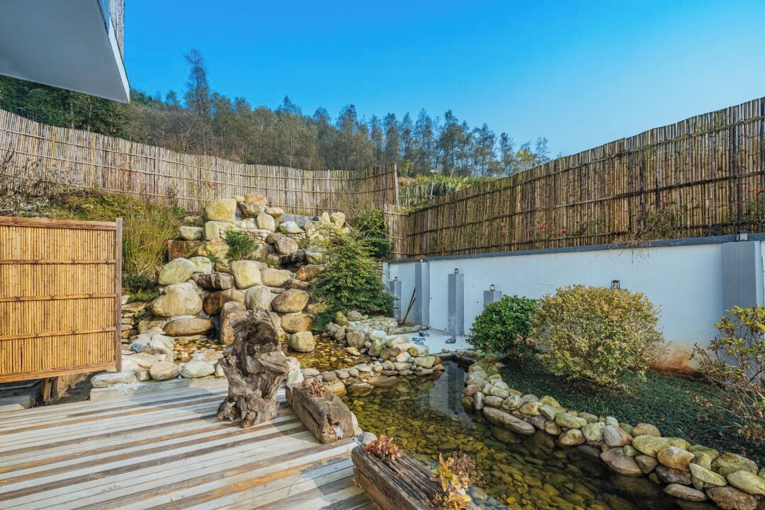 A serene garden with a wooden deck, stone formations, and a bamboo fence.
