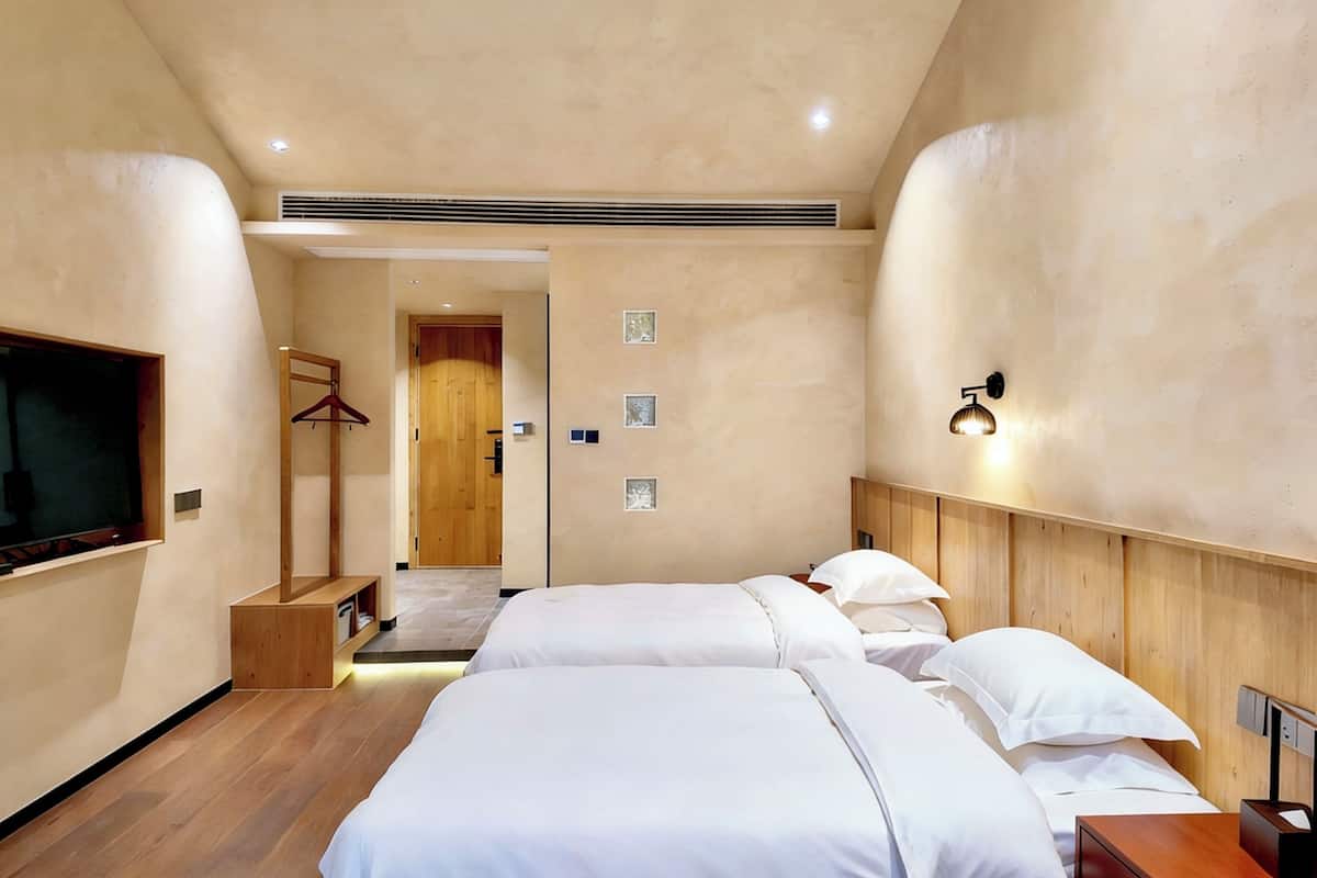 A hotel room with two beds, a TV, a wooden wardrobe, a coat rack, and a hallway leading to a door.