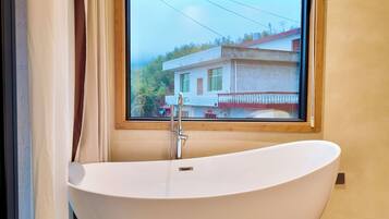 A modern bathroom with a freestanding bathtub, a window with a view of a house, and a wooden-framed window.